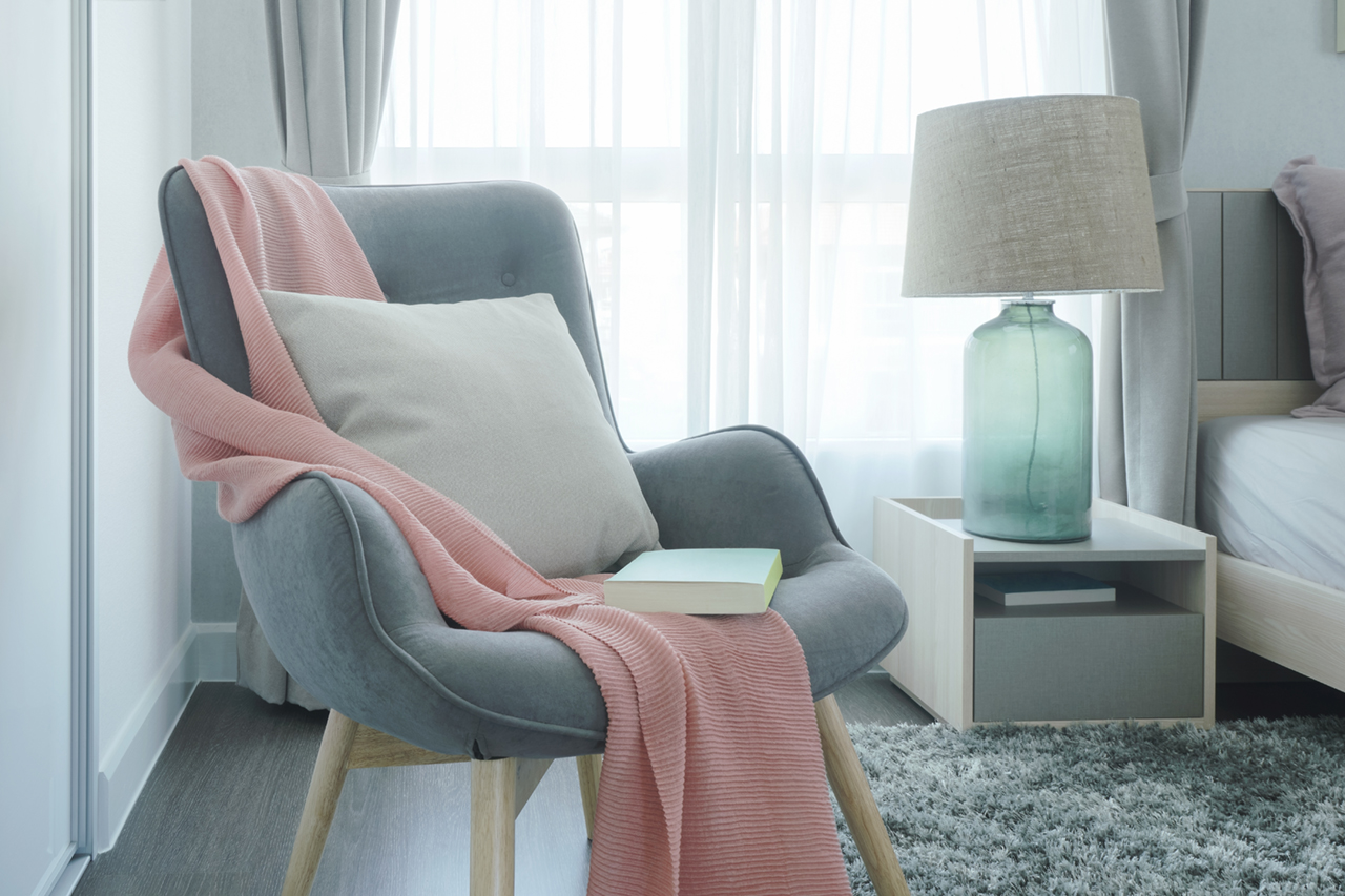 Gray easy armchair with pink scarf, pillow and book next to bed in the bedroom