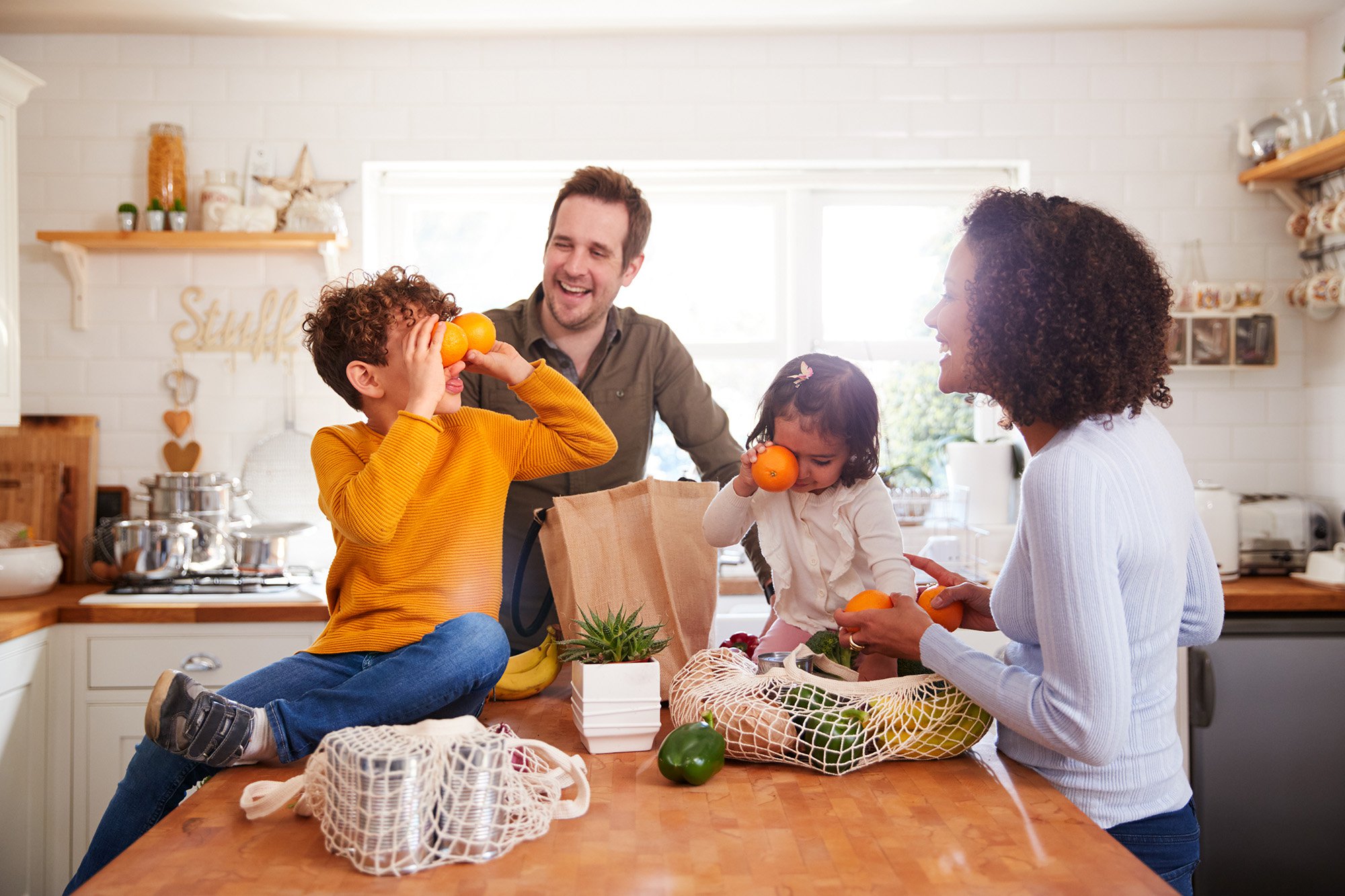 Family Returning Home From Shopping Trip Using Plastic Free Bags Unpacking Groceries In Kitchen stock photo